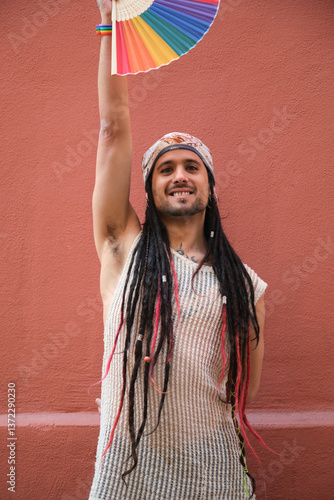 Obraz na płótnie Portrait of smiling young man with dreadlocks and bandana raising rainbow hand fan supporting LGBT community w salonie