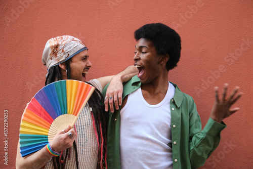 Obraz na płótnie Two male friends are laughing and having fun together while celebrating LGBT pride, one of them is holding a rainbow fan w salonie