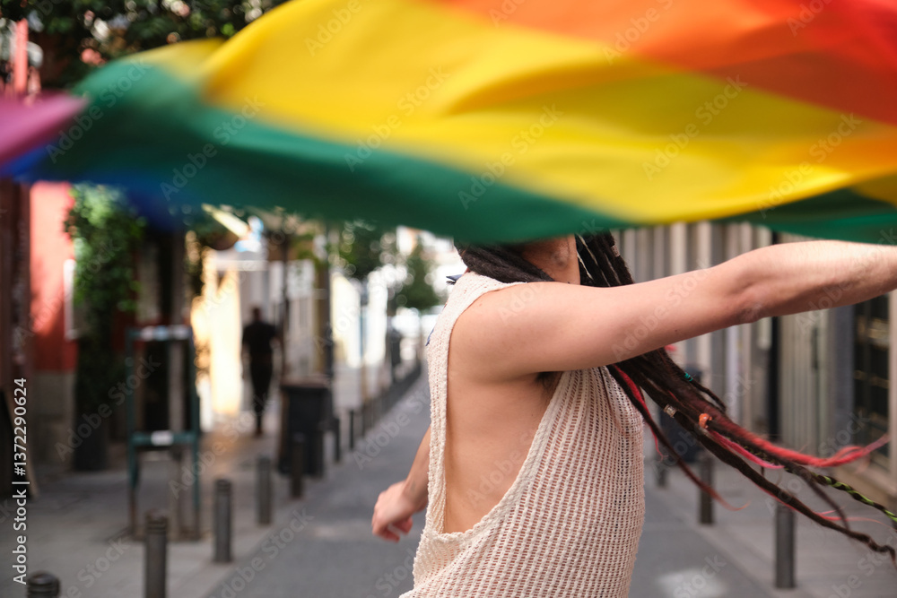 Young man with dreadlocks waving rainbow flag celebrating LGBT pride in the street