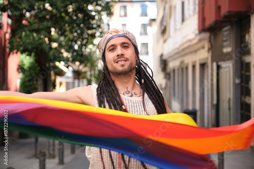Young artist with dreadlocks holding rainbow flag celebrating LGBT pride in the city