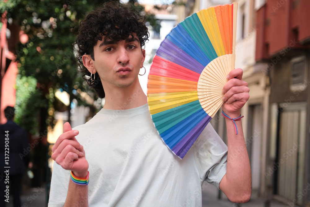 Young man showing rainbow fan and making heart sign with fingers celebrating LGBT pride in the city