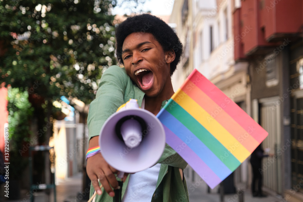 Young man holding rainbow flag and shouting with megaphone at a lgbt pride parade promoting equal rights