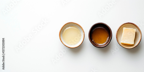 Three ceramic bowls with cooking fats: melted lard, ghee and a block of solid animal fat on white background