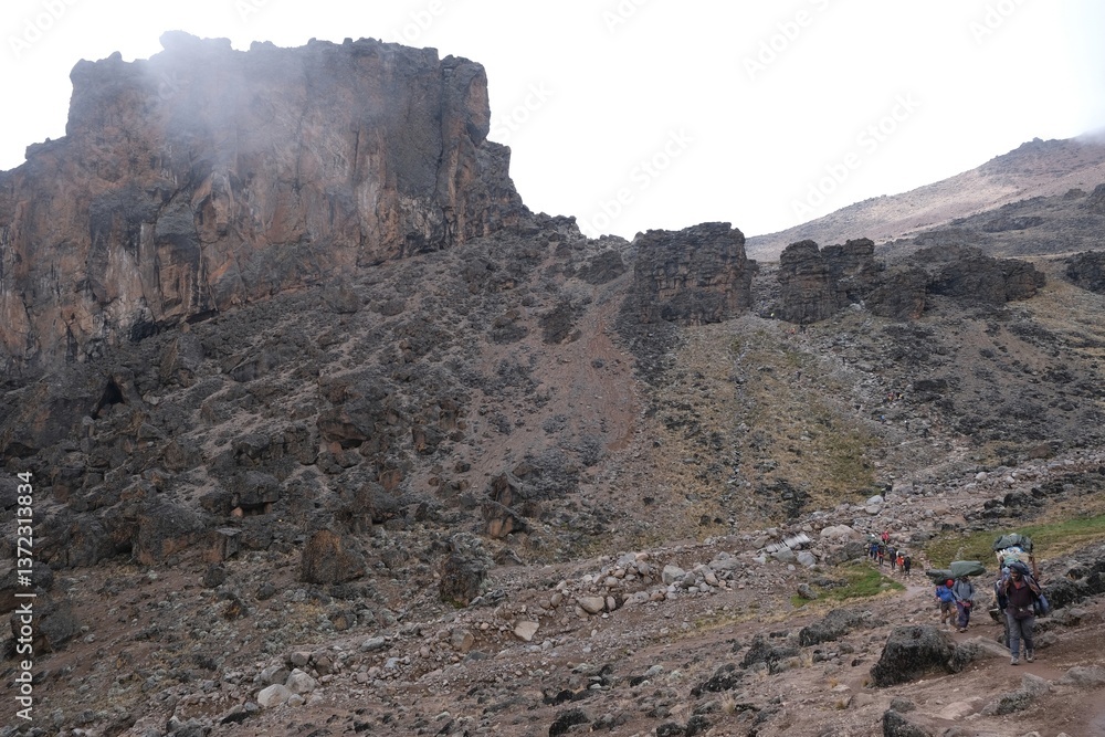 Kilimanjaro, Tanzania: Misty scenery of Lava Tower and silhouettes of trekking people. Machame Route, trail from Shira Camp to Barranco Camp.