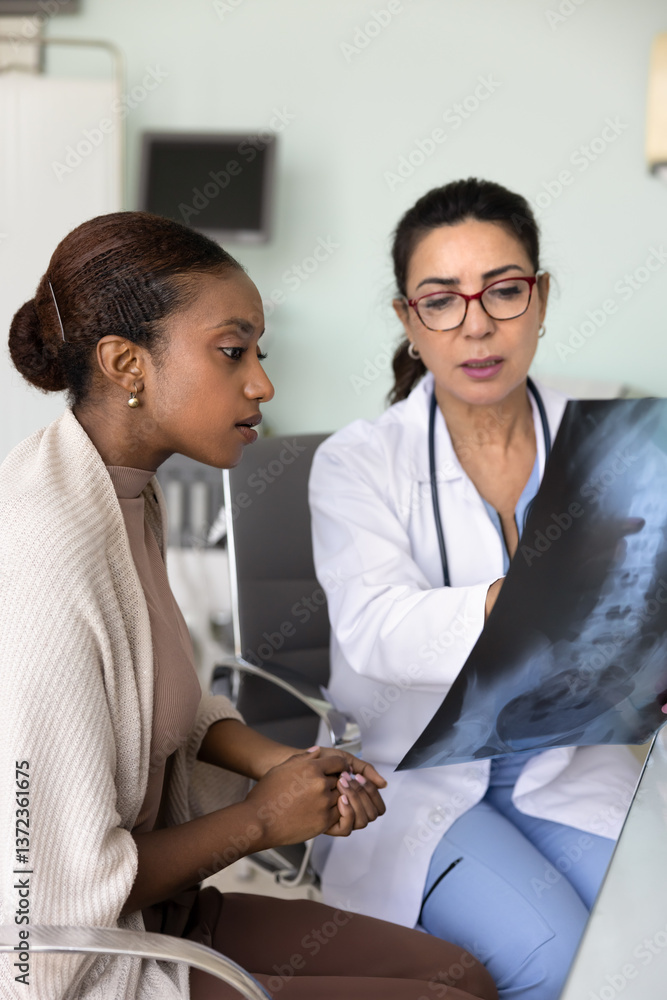 Obraz premium Senior neurologist doctor showing Xray shot of spine bones to young African patient woman, pointing at scan, explaining examination result, diagnosis, roentgen image