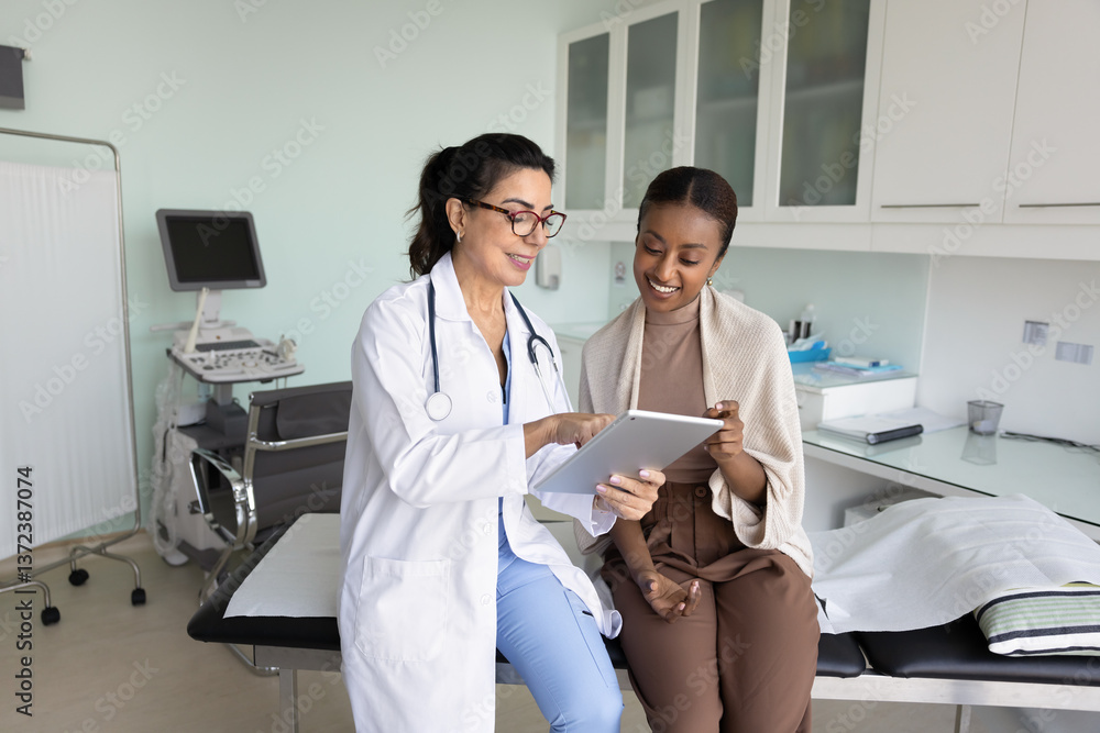 Obraz premium Positive senior ultrasonography doctor showing ultrasound examination results to young African female patient, explaining medical checkup electronic result, telling good news, smiling