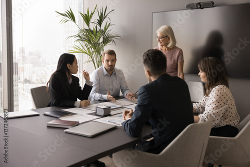 Papier peint Millennial businessman addressing group of professionals seated together at tabl