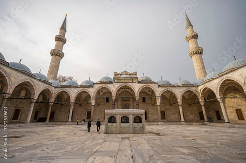 Majestic view of the inner courtyard of the Süleymaniye Mosque in Istanbul showcasing its grand arches, domes, and towering minarets under a serene sky with a few visitors admiring the architecture