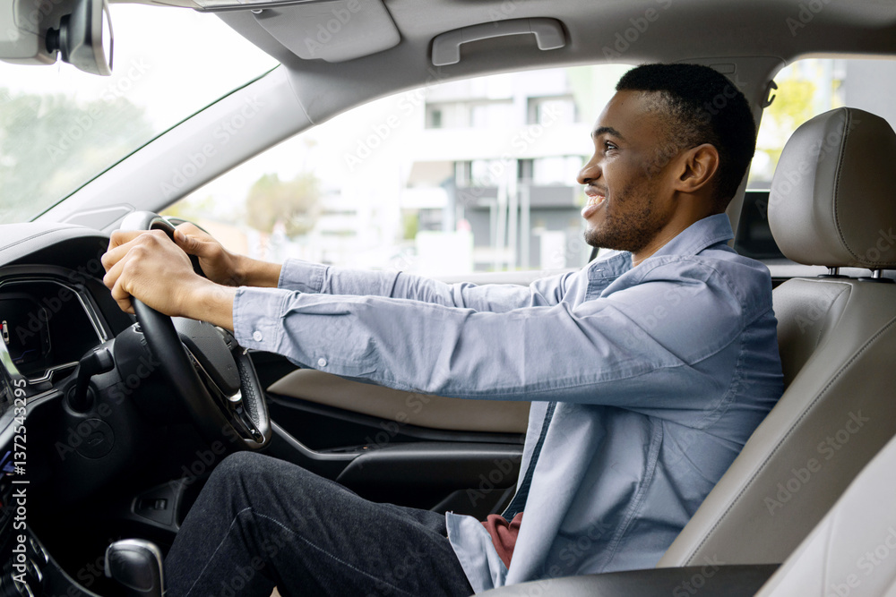 Side view shot of black guy driving his automobile, sitting on drivers seat and holding steering wheel, looking at road Side view shot of black guy driving his automobile, sitting on drivers seat and holding steering wheel, looking at road