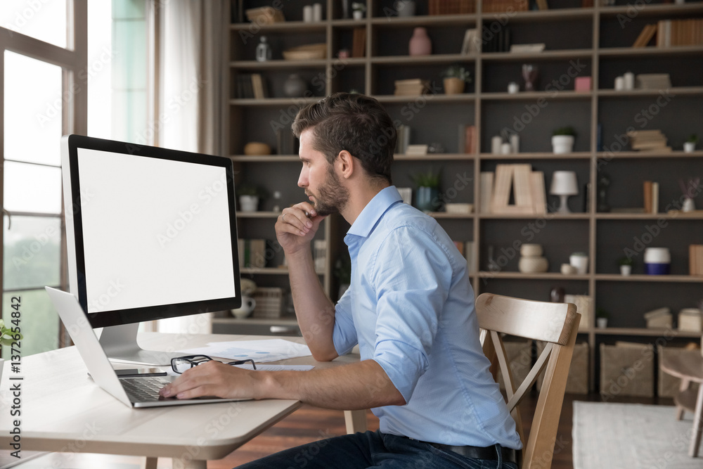 Thinking on information. Thoughtful millennial businessman entrepreneur student project developer working from home office looking at blank desktop pc screen with copyspace for mockup using notebook Thinking on information. Thoughtful millennial businessman entrepreneur student project developer working from home office looking at blank desktop pc screen with copyspace for mockup using notebook