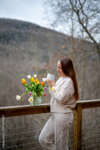 Young woman enjoys a cup of tea with a bouquet of tulips on a mountain deck in early spring