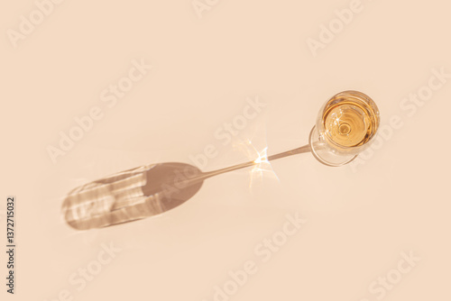 White wine in crystal transparent glass with shadow and glare at sunlight, light white beige background, creative summer alcohol drink minimal concept, copy space, top view, pastel peach color