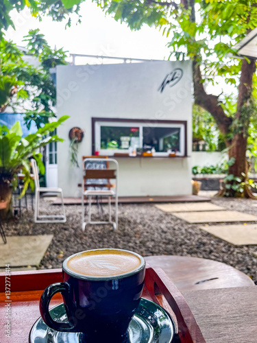 Obraz na płótnie Outdoor café features a small white building with a service window, surrounded by lush trees and greenery. Stone pavers lead to cozy seating areas, creating a relaxed and natural atmosphere. w salonie