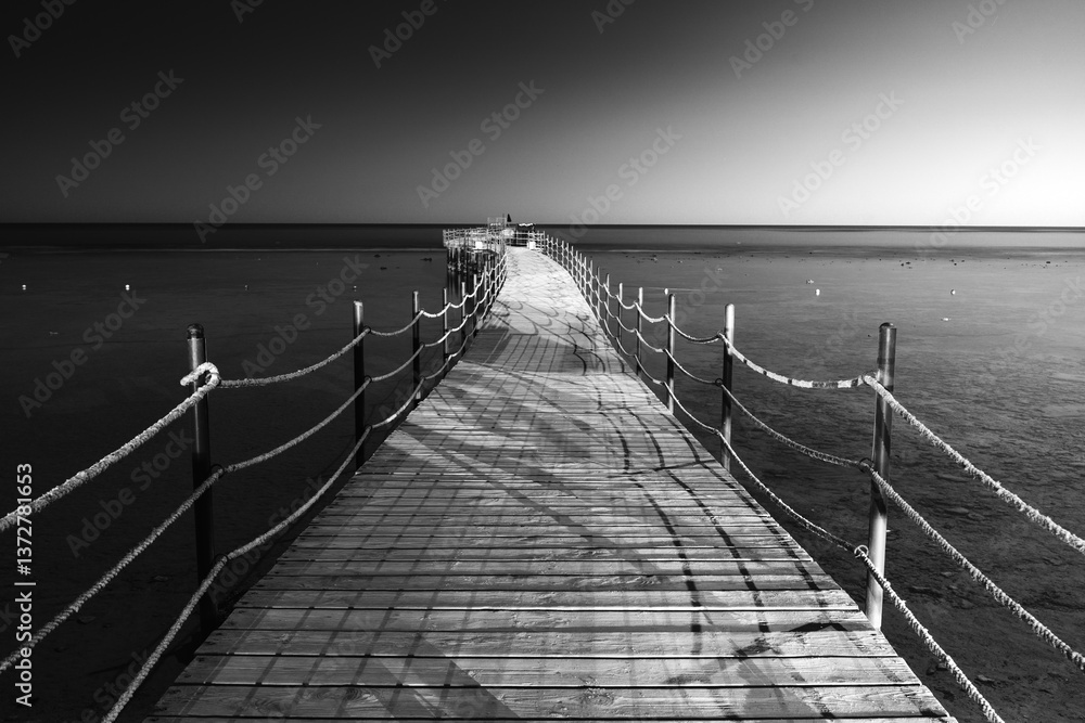 Fototapeta premium Drewniany pomost prowadzący do morza, czarno-białe zdjęcie o nostalgicznej atmosferze 