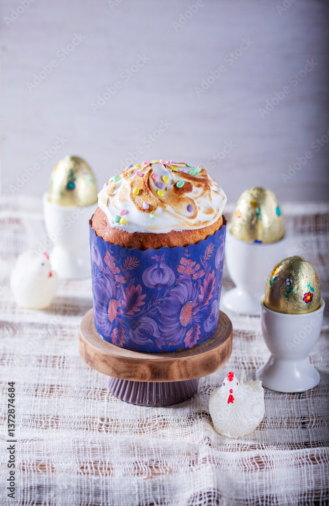 Easter cake, chocolate eggs in gold foil and chicken-shaped candles on a light background.