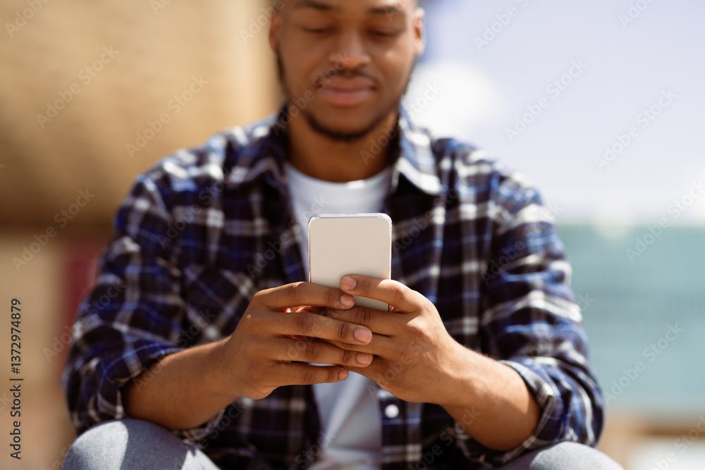 Technology Concept. Closeup portrait of afro person using cell phone, sitting outdoors, selective focus on device Technology Concept. Closeup portrait of afro person using cell phone, sitting outdoors, selective focus on device