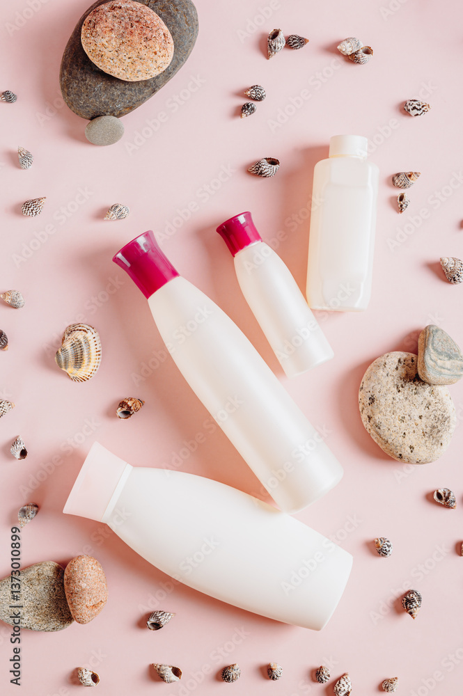 Set of bottles with cosmetic products among stones and shells on pink top and vertical view