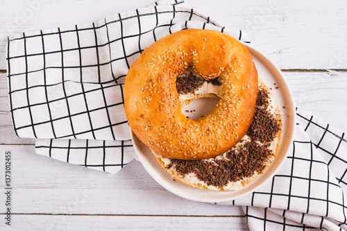 Close up of bagel sandwich with butter and grated chocolate on a plate on a table top view