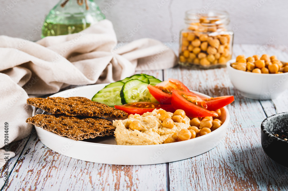 Hummus, chickpeas, tomato, cucumber, grain crackers on a plate on the table