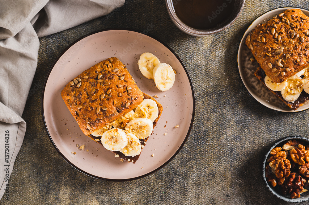 Sweet sandwich with chocolate butter, banana and nuts on a plate on the table top view