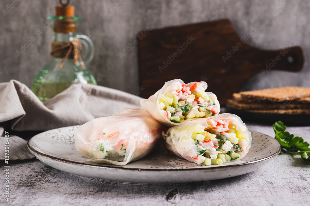 Spring rolls in rice paper with crab sticks, cucumber, greens and sauce on a plate on the table