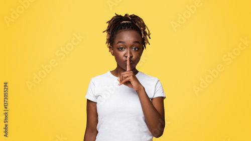 Fotografie Pretty silent black woman making hush gesture, yellow studio background with copy space