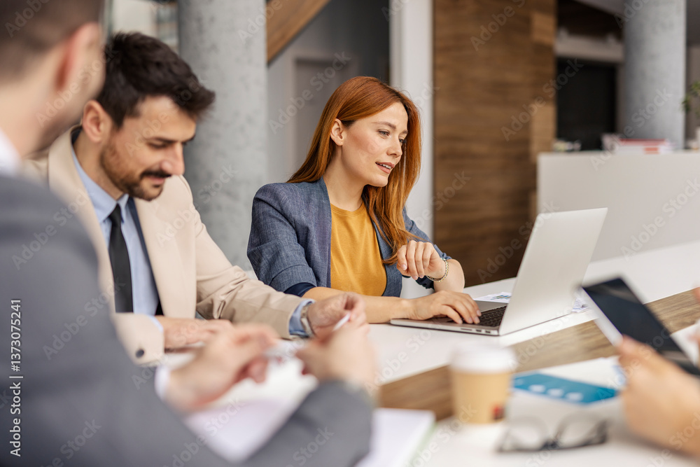 Portrait of businesswoman sitting at boardroom and using laptop while her team of experts analyzing data. Portrait of businesswoman sitting at boardroom and using laptop while her team of experts analyzing data.