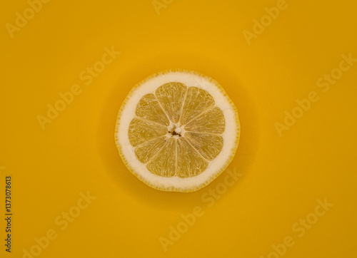 A fresh lemon slice on a vibrant yellow background