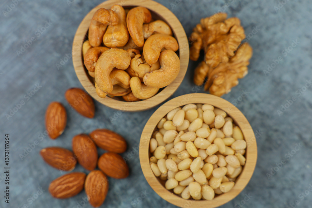 Close-up view from above of wooden bowls with pine nuts and cashews, which stand on the side surrounded by walnuts and almonds on a gray background. The concept of healthy snacks, healthy and Close-up view from above of wooden bowls with pine nuts and cashews, which stand on the side surrounded by walnuts and almonds on a gray background. The concept of healthy snacks, healthy and