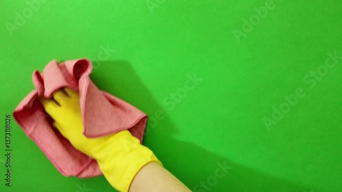 A hand in a yellow rubber glove wipes the window glass with a pink cloth. Housework and housekeeping. Close-up. Green screen, chroma key