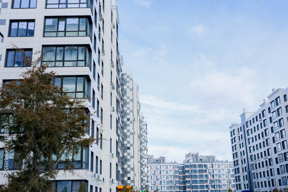 Obraz premium A residential complex with houses of modern architecture in white with gray inserts, large balconies and windows against the blue sky. The concept of apartments for living, city, area of residence