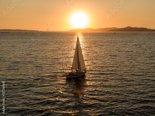 Photography A sailboat with three people aboard glides across the water at sunset in  San Francisc, California, USA