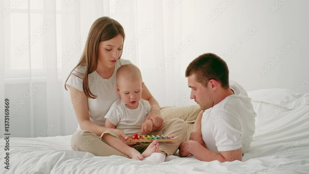 A young child engages with colorful toys as both parents sit beside him on a soft bed. The room is filled with natural light, creating a warm and nurturing atmosphere. A young child engages with colorful toys as both parents sit beside him on a soft bed. The room is filled with natural light, creating a warm and nurturing atmosphere.