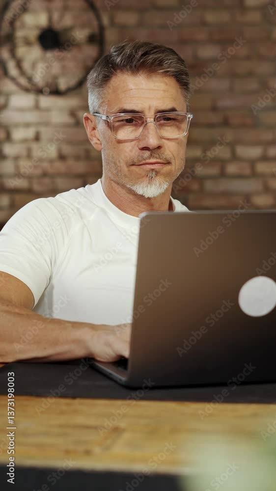 Man drinking coffee at desk in loft apartment, preparing for long business day. Businessman in casual cloth working on laptop in home office. Portrait of happy male entrepreneur smiling. Man drinking coffee at desk in loft apartment, preparing for long business day. Businessman in casual cloth working on laptop in home office. Portrait of happy male entrepreneur smiling.