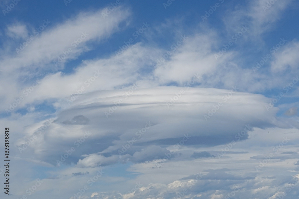 A striking, circular cloud formation is visible against a bright blue sky filled with soft white clouds. This unusual weather pattern creates a captivating view during the afternoon hours