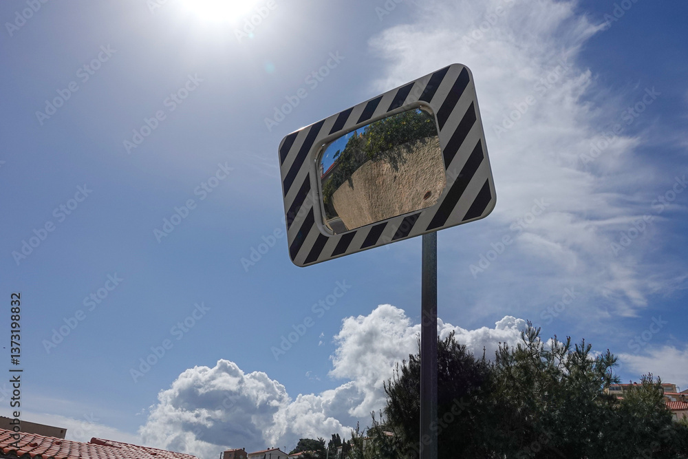 A roadside mirror reflects greenery and a bright blue sky filled with fluffy clouds.