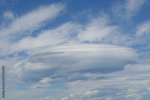 Obraz na płótnie A striking, circular cloud formation is visible against a bright blue sky filled with soft white clouds. This unusual weather pattern creates a captivating view during the afternoon hours w salonie