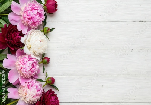 Elegant peonies in shades of pink and red are arranged on a white wooden background.