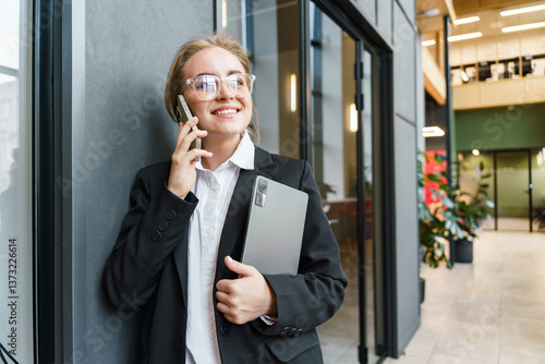 Wallpaper Mural Confident professional woman talking on the phone while holding a laptop in a modern office Torontodigital.ca