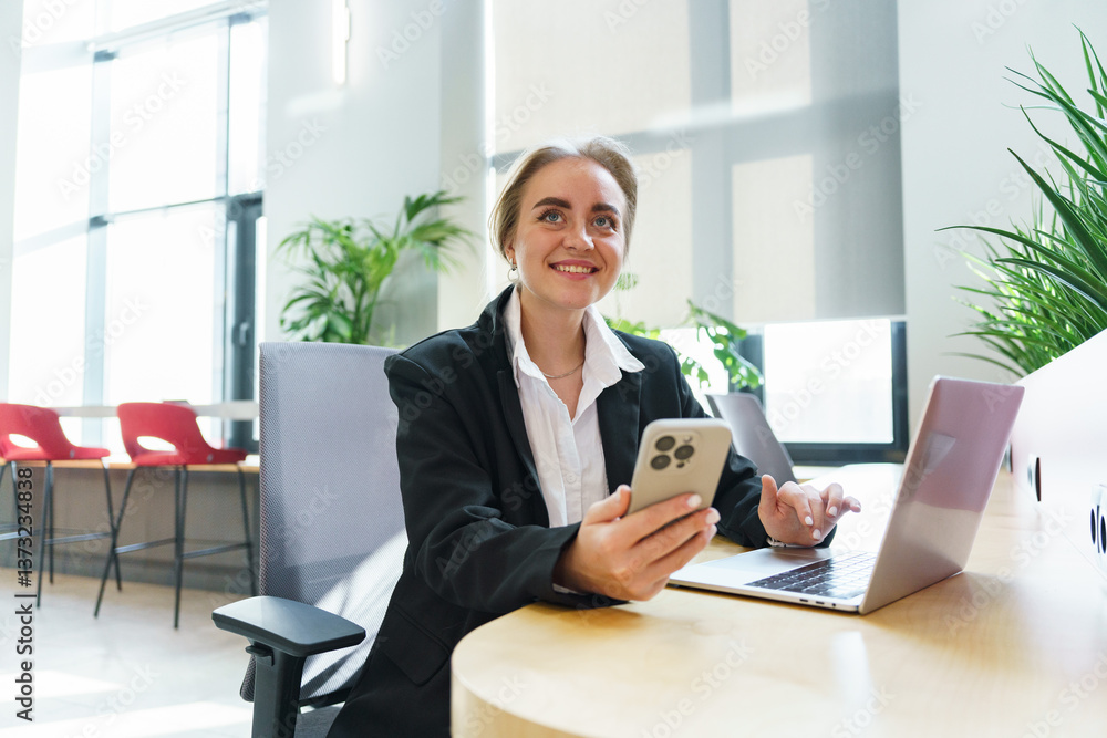 Professional woman working at a desk in modern office space, using laptop and smartphone Professional woman working at a desk in modern office space, using laptop and smartphone