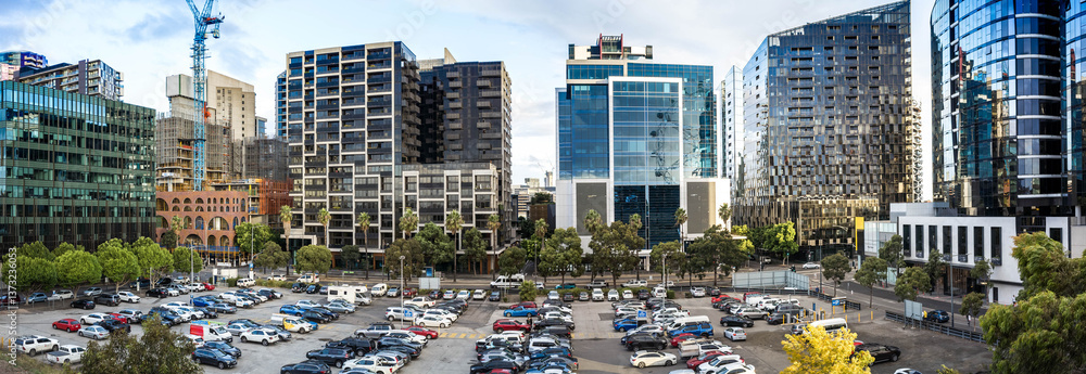 Fototapeta premium Panoramic view of multiple modern high-rise apartment buildings and office towers, with a large urban parking lot full of parked cars, in Melbourne, Australia
