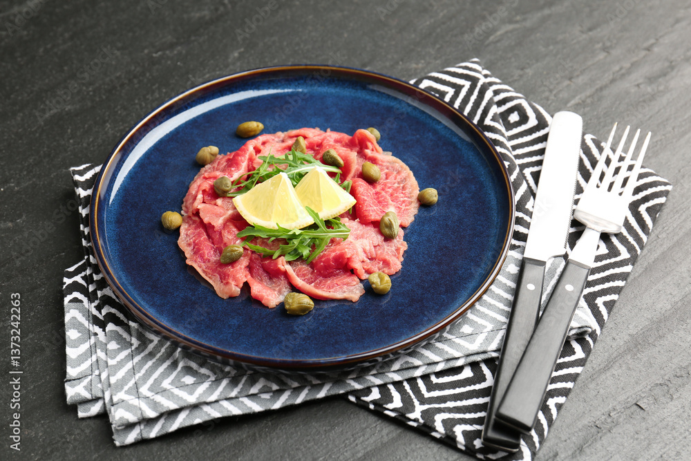Fresh beef carpaccio with arugula, lemon and capers on dark textured table, closeup Fresh beef carpaccio with arugula, lemon and capers on dark textured table, closeup