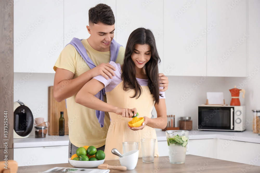 Happy young couple squeezing lime juice for mojito in kitchen Happy young couple squeezing lime juice for mojito in kitchen