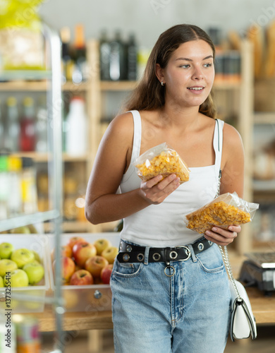 Young female shopper chooses corn flakes in package in grocery store