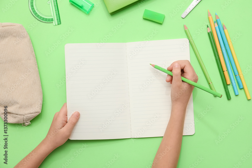 Child's hands writing down something in notebook on green background. Top view Child's hands writing down something in notebook on green background. Top view