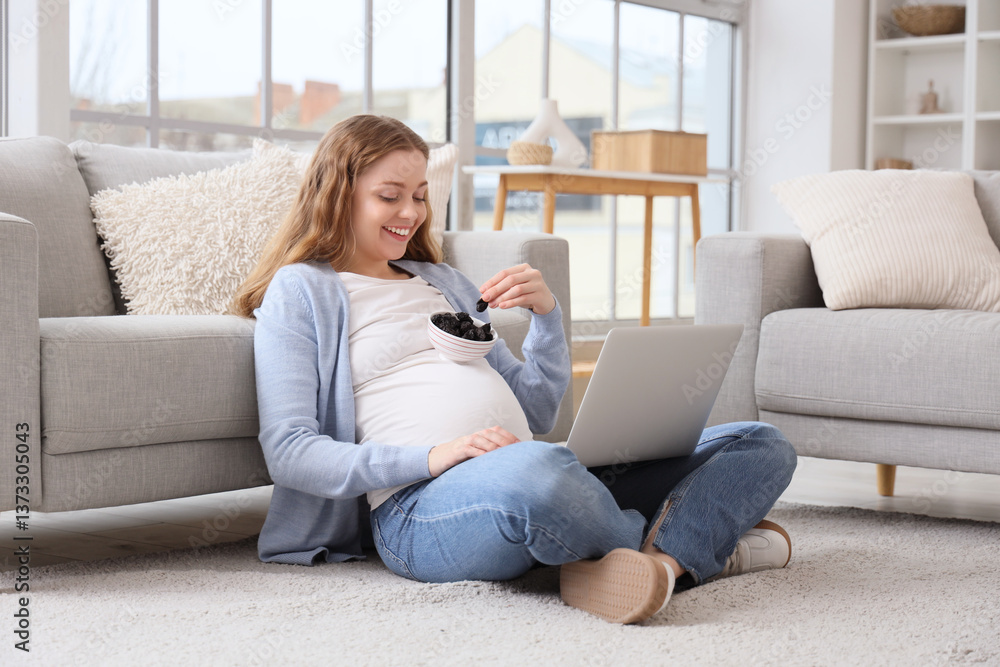 Obraz premium Young pregnant woman with dried prunes using laptop at home