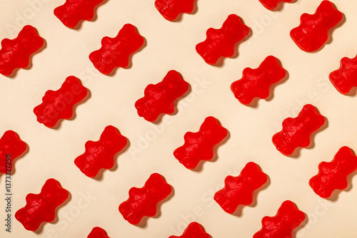 Vibrant red gummy bears are laid out in a uniform pattern against a soft, light background