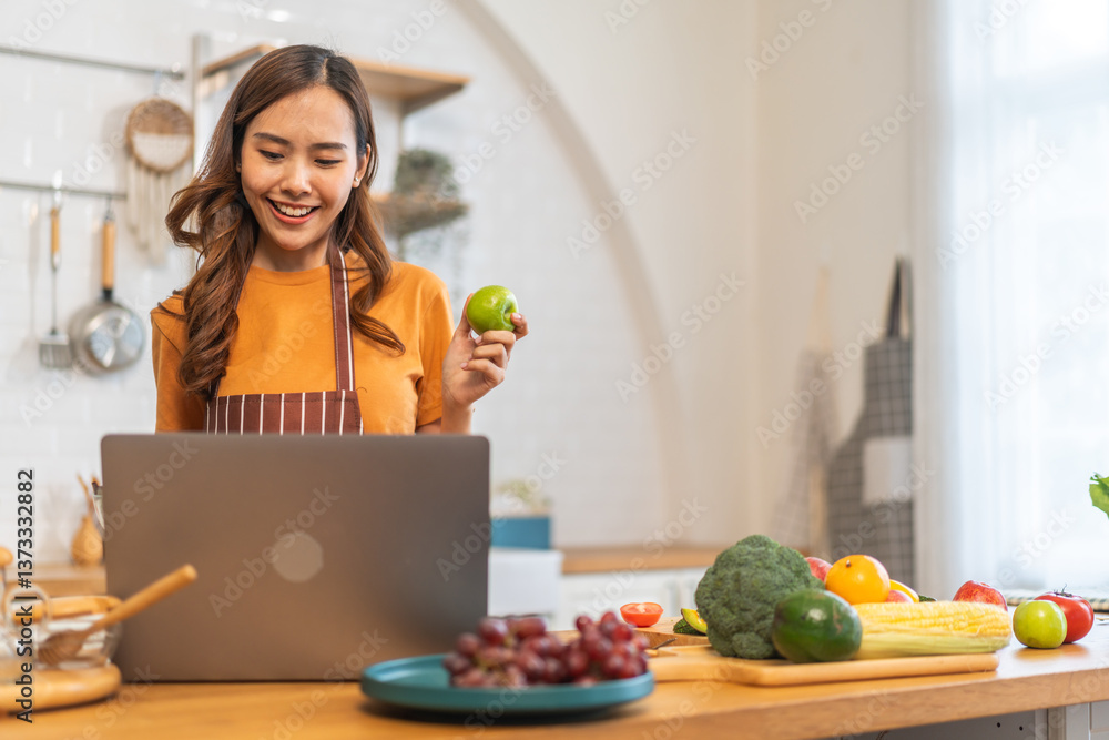 Asian young woman holds laptop with online audience or simply enjoying the cooking process, health, fruit, freshness, and organic living, digital recipe platform, eating, healthy at kitchen Asian young woman holds laptop with online audience or simply enjoying the cooking process, health, fruit, freshness, and organic living, digital recipe platform, eating, healthy at kitchen