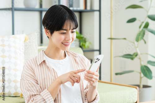 Foto リビングでスマホを使う若い女性