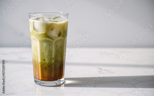 Wallpaper Mural Tall glass of iced matcha latte with green tea and milk layers, topped with ice cubes, on white marble surface in bright sunlight. Torontodigital.ca